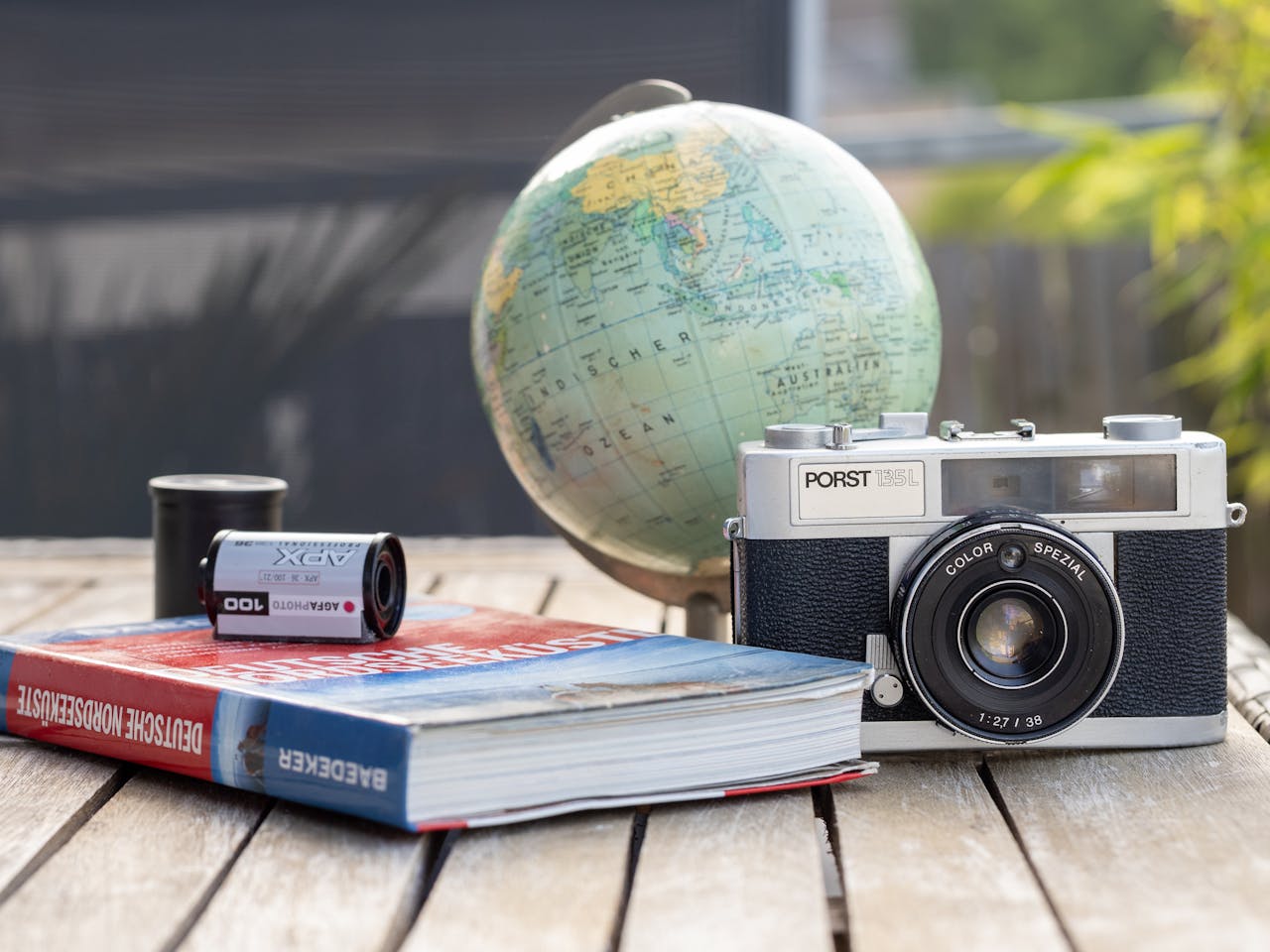 A vintage camera with a globe and book on a wooden table, ideal for travel and photography themes.