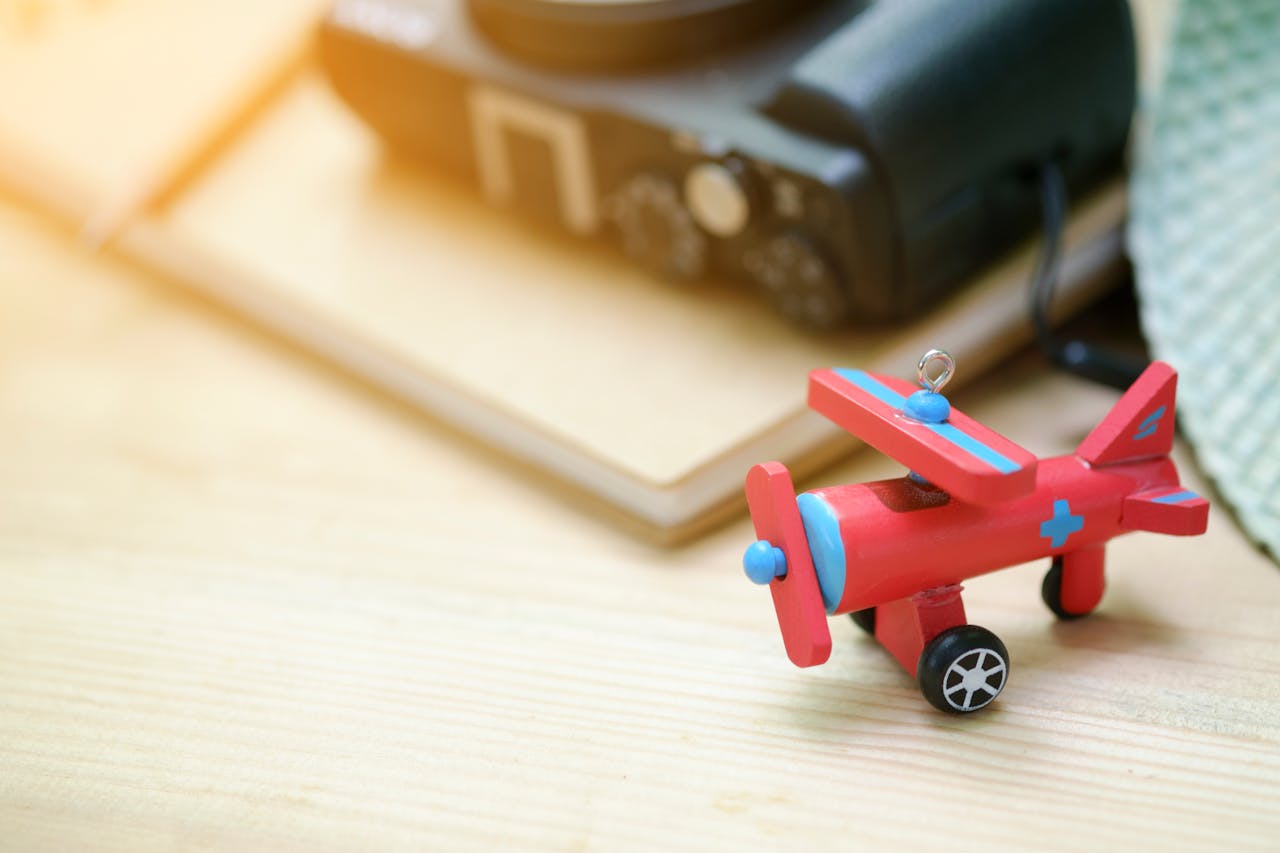 Colorful wooden toy airplane beside a digital camera on a wooden surface.