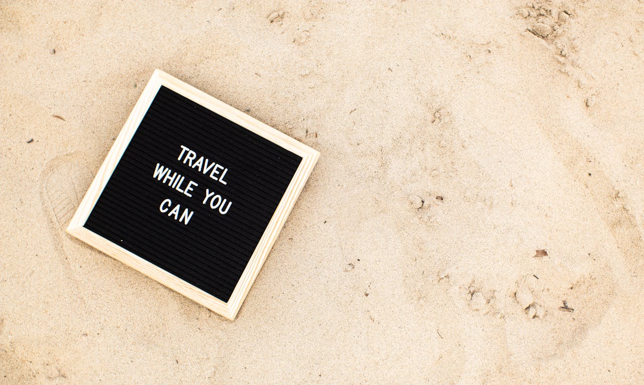 Letter board with 'Travel While You Can' message displayed on sandy beach scene, inspiring wanderlust.